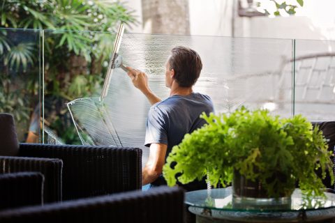 man-in-gray-shirt-cleaning-clear-glass-wall-near-sofa-713297